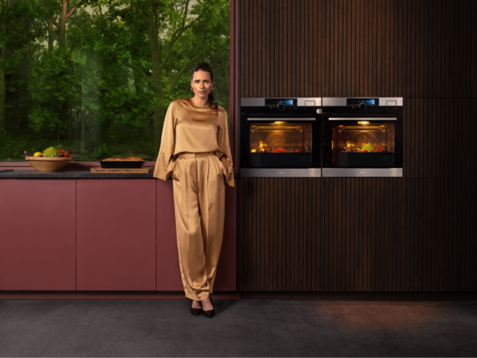 Woman standing next to two ovens in a kitchen.